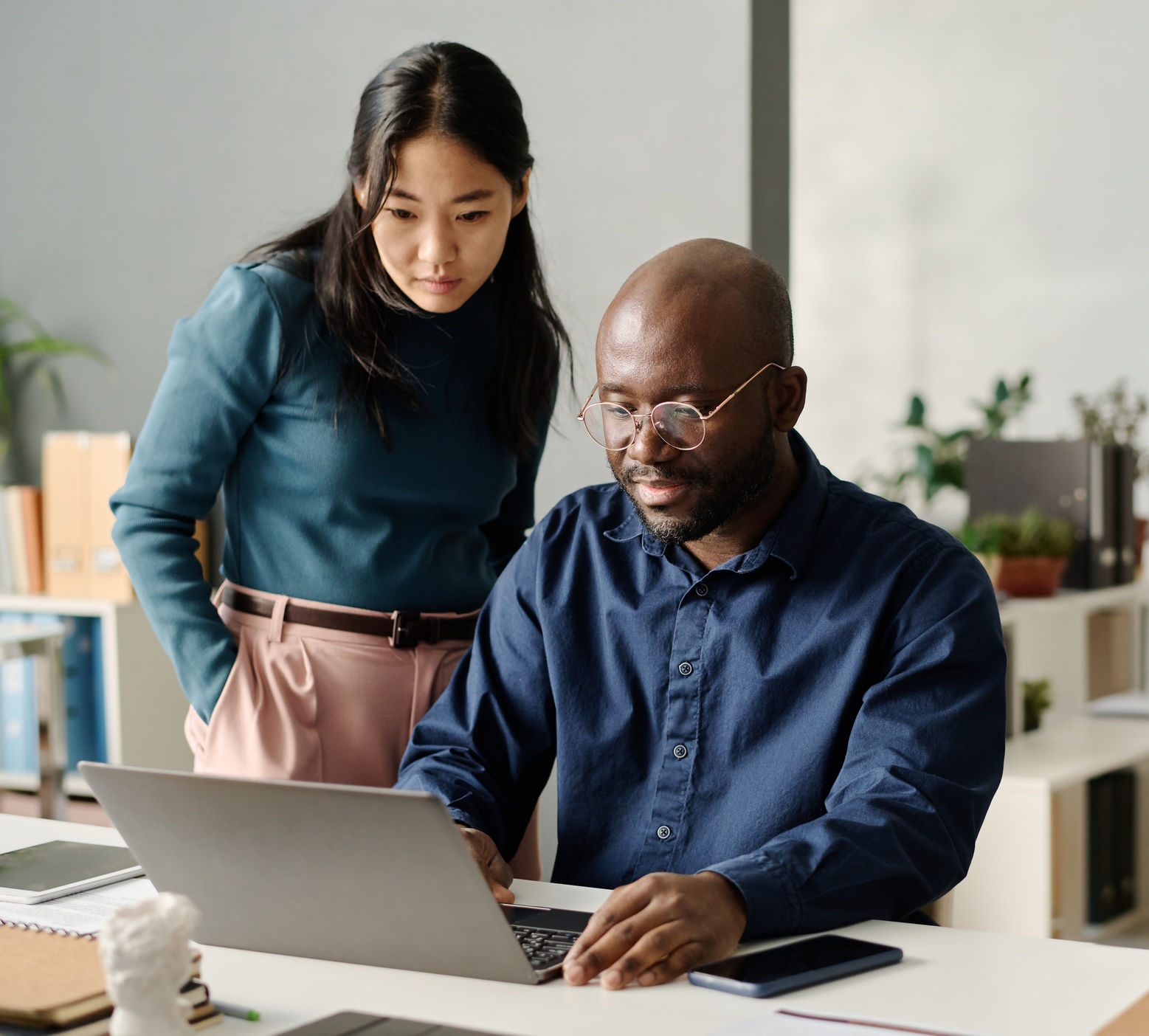 Asian Woman And Black Man Looking At Laptop Screen Young African American man working on presentation design on laptop showing it to his Asian coworker, copy space